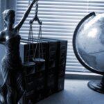 Justitia Skulptur, Gesetzestexte und Globus auf Schreibtisch