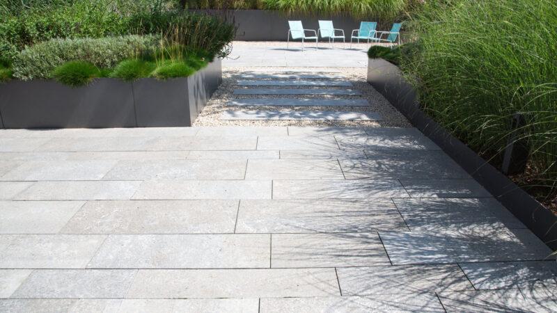 Moderne Garten- und Terrassengestaltung mit Natursteinplatten: Terrasse und Gehweg aus Natursteinplatten, umgeben von Schotter und Metall Pflanzgefäßen mit Grünpflanzen
