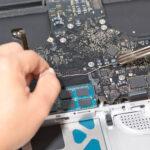Technische Reparatur eines Laptops, ein Mann lötet das Mainboard eines Macbooks