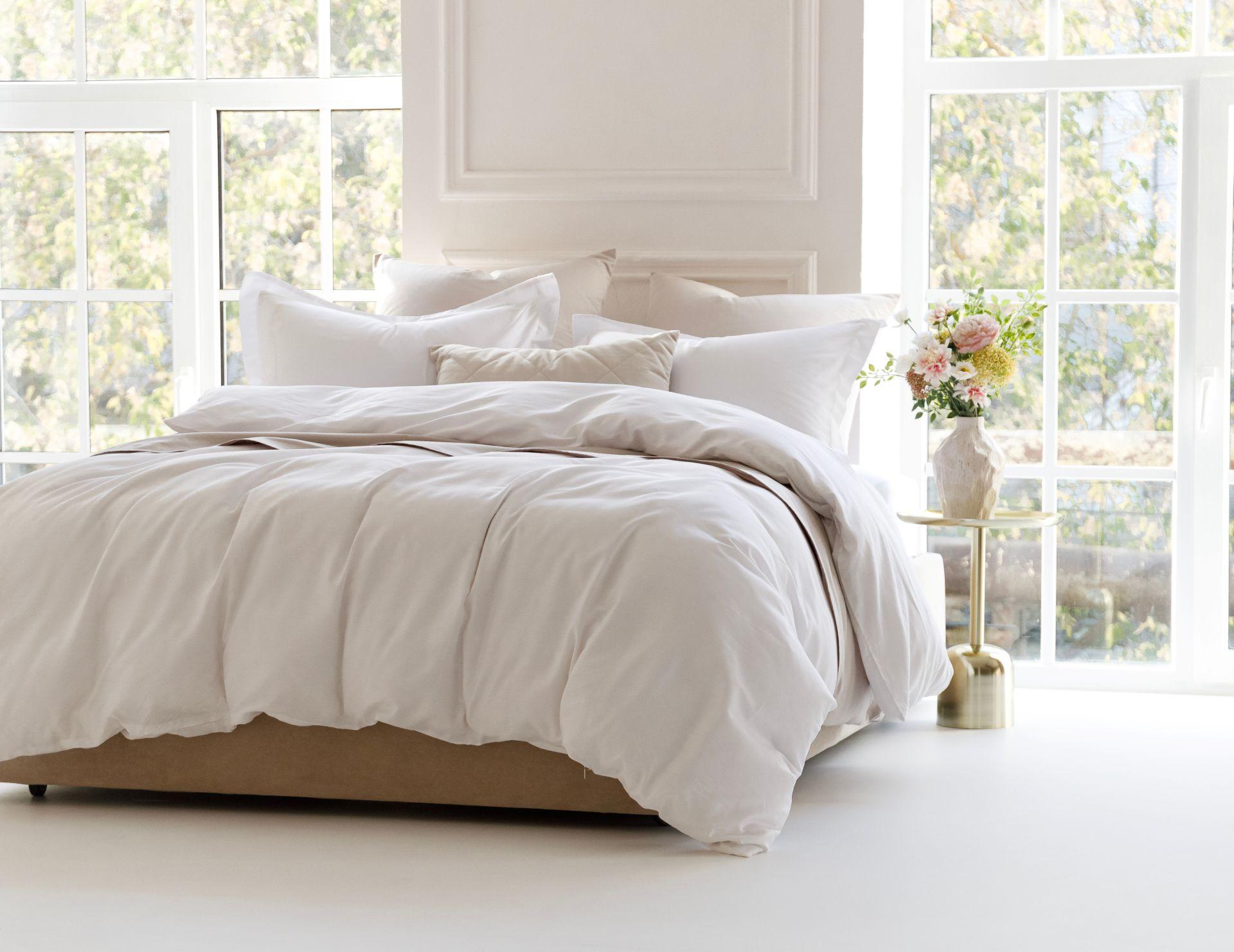 Helles Schlafzimmer mit einer weißen Alpaka Bettdecke und frischen Blumen, Symbol für Natürlichkeit, Komfort und nachhaltige Einrichtung.